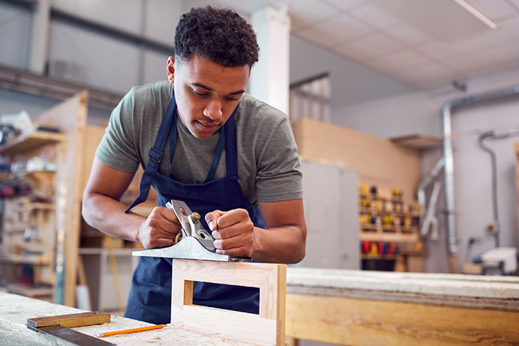 man using a planar against a wooden frame