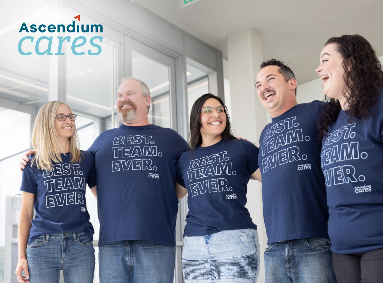 Five Ascendium employees stand shoulder to shoulder smiling wearing t-shirts that say best team ever