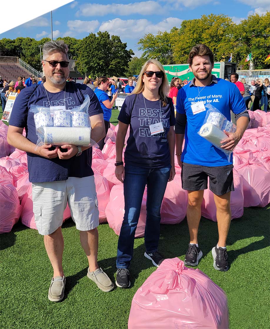 Three employees pose in a football field surrounded by bags filled with products they helped collect.